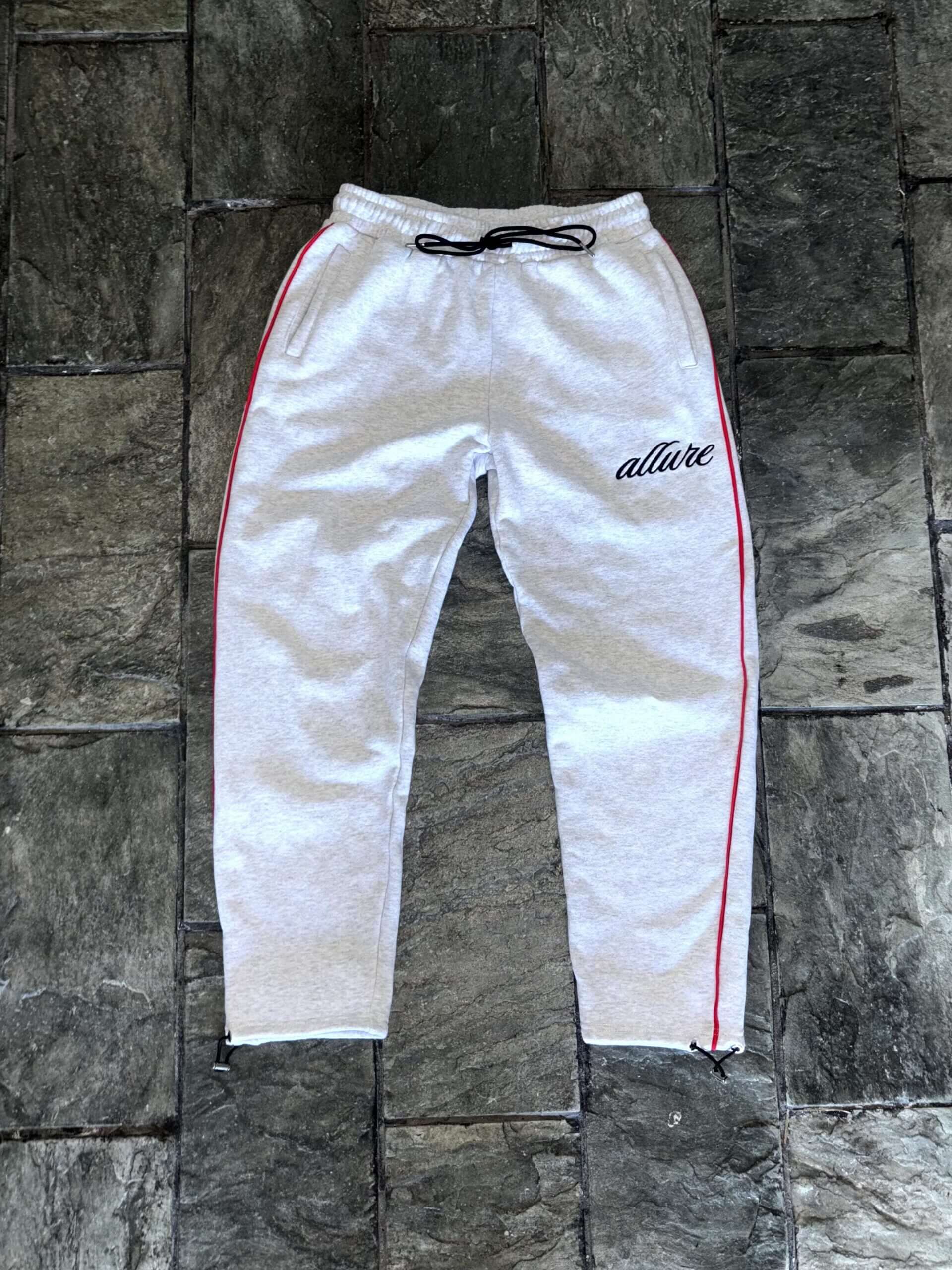 Allure Track Pants in grey, featuring red stripes, drawstrings, and luxury slim fit for comfort and style.
