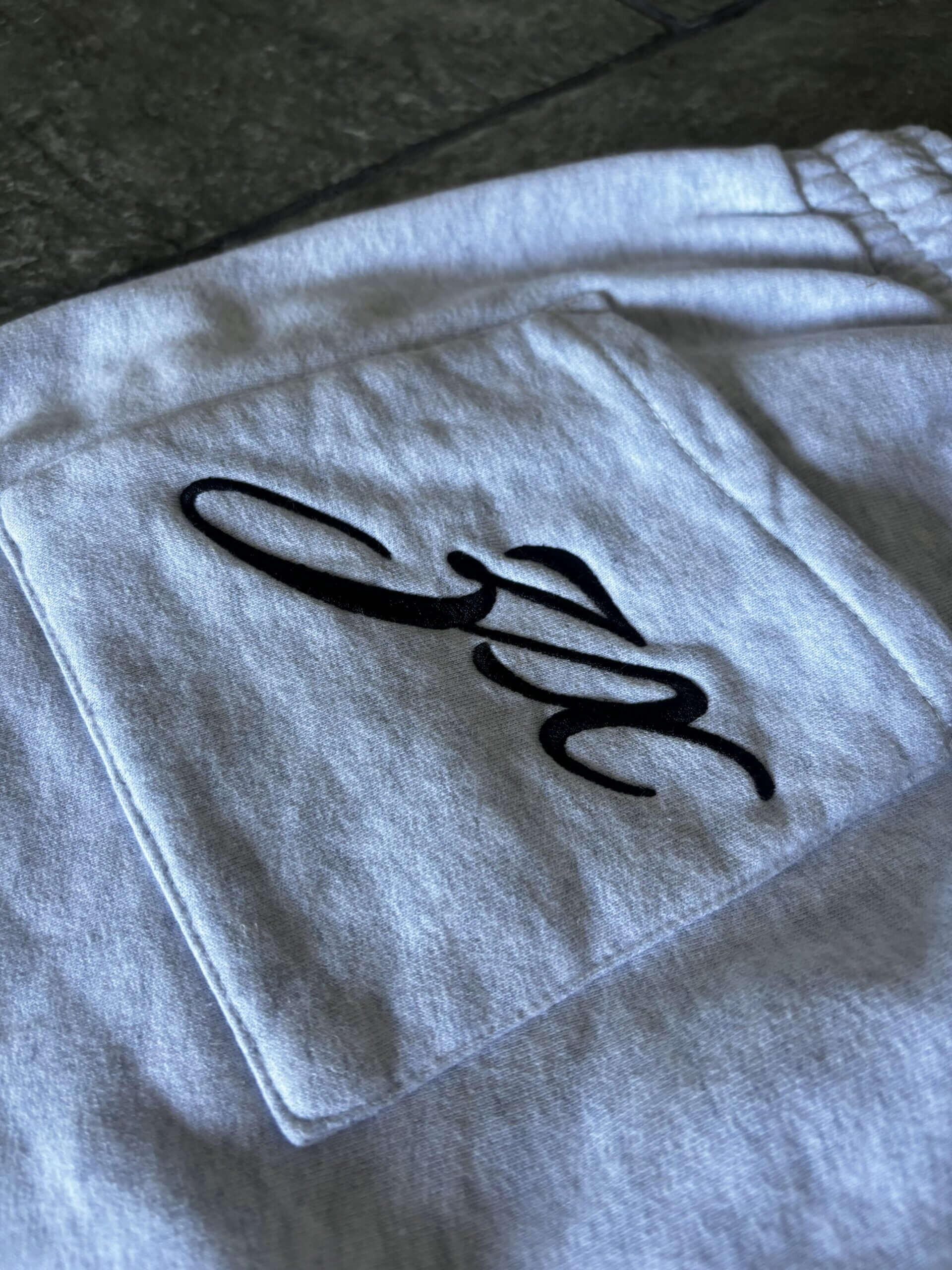 Close-up of Allure Track Pants featuring black embroidery on a grey cotton rear pocket.